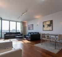 Nappali nagy ablakokkal, fa dekorációjú padlóval, kényelmes bútorokkal és étkező sarokkal.