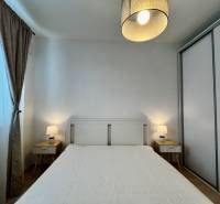 Hálószoba egy kétszobás lakásban fehér ággyal, éjjeliszekrényekkel és lámpákkal.