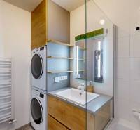 Fürdőszoba egy háromszobás lakásban mosógéppel, szárítógéppel, mosdóval és üveg zuhanykabinnal.