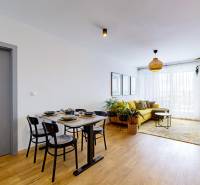 Nappali egy háromszobás lakásban, fa mintázatú padlóval, sárga kanapéval és étkezőasztallal.