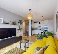 Nappali sárga kanapéval, fali dekorációkkal és fa mintázatú padlóval egy háromszobás lakásban.