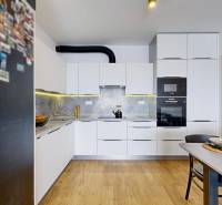 Konyha egy háromszobás lakásban fehér szekrényekkel és fa mintázatú padlóval.