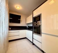 Fehér konyha fekete akcentusokkal és készülékekkel egy kétszobás lakásban.