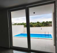 Kilátás a családi házból a teraszra medencével, fa dekorációjú padlóval.