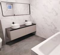 Családi ház fürdőszobája ovális mosdókkal, tükörrel és káddal.