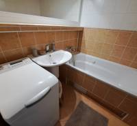 Fürdőszoba egy háromszobás lakásban káddal, mosdóval és mosógéppel, narancssárga csempékkel burkolt padlóval.