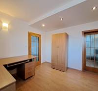 Szoba egy négy szobás lakásban fa mintás padlóval, asztallal és szekrénnyel.