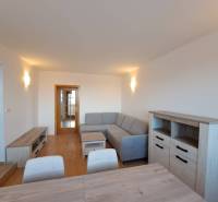 Nappali egy négy szobás lakásban fa mintázatú padlóval és szürke kanapéval.