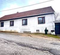 Családi ház Unínban fehér homlokzattal, barna tetővel és bekötőúttal.