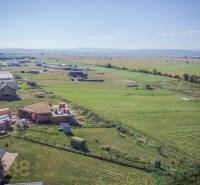 Telkek - lakóhely Mlynicában; épülő házak és kiterjedt mezők a napos égbolt alatt.