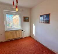 Szoba egy családi házban, szőnyeggel borított padló, fehér radiátor, képek a falakon.