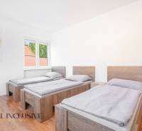 Három ágy a szobában fa mintázatú padlóval és egy képpel a falon.