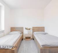 Szoba két ággyal, éjjeliszekrénnyel és fa mintázatú padlóval.