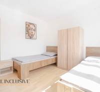 Hálószoba két ággyal és bútorokkal, fa mintázatú padló, kép a falon.