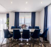 Ebédlő a villában sötét függönyökkel, fa mintázatú padlóval és kék székekkel.