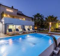 Villa Kaštelában megvilágított medencével, napozóágyakkal és pálmafákkal a kertben alkonyatkor.