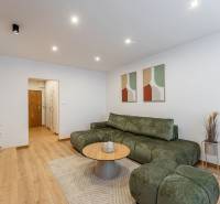 Nappali egy kétszobás lakásban fa dekor padlóval, zöld kanapé, dohányzóasztal.