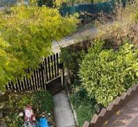 Kert a ház mellett Felsővályban, sétánnyal, zöldterülettel és kerti dekorációval.