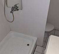 Fürdőszoba egy egyszobás lakásban fehér csempével és zuhanyzóval.