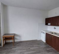 Konyha egy egyszobás lakásban sötét szekrényekkel és fa dekorációjú padlóval.