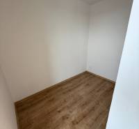 Üres szoba egy egyszobás lakásban, fa mintázatú padlóval, fehér falakkal.