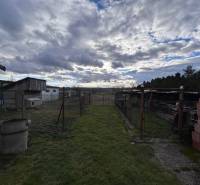 Kilátás egy zbehi családi ház kertjére felhős éggel és gazdasági melléképületekkel.