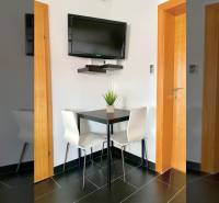 Ebédlő egy családi házban sarokasztallal, falra szerelt televízióval és fekete csempékkel.