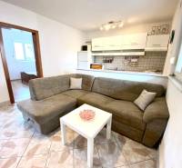 Családi ház belső tere kanapéval, fehér asztallal és konyhasarokkal.