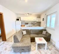 Nappali családi házban kanapéval és konyhasarokkal, padlón csempe.