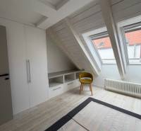 Tetőtéri szoba fa dekorációs padlóval, beépített szekrénnyel és sárga székkel.