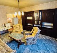 Nappali egy kétszobás lakásban régebbi bútorokkal és szőnyeggel a padlón.