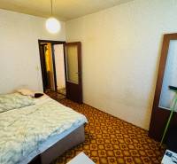 Hálószoba szőnyeggel, ággyal és világos falakkal egy kétszobás lakásban.