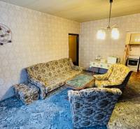 Nappali retro ülőgarnitúrával, mintás szőnyeggel, bejárat a konyhába egy kétszobás lakásban.