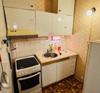 Konyha egy kétszobás lakásban, fehér szekrények, tűzhely, mosogató, fa dekoros padló.