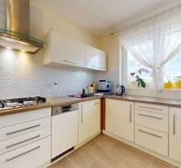 Konyha családi házban fehér szekrényekkel, hűtőszekrénnyel és nagy ablakkal.