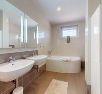 Családi ház fürdőszobája dupla mosdóval, káddal és kerámia burkolattal.