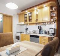 Konyha egy 3 szobás lakásban világos konyhabútorral, háztartási gépekkel és asztallal székekkel.