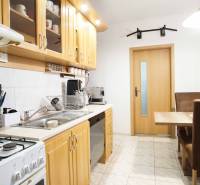 Konyha egy háromszobás lakásban fa szekrényekkel és étkezőasztallal.