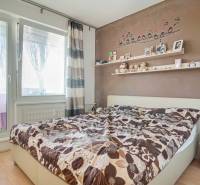 Hálószoba egy háromszobás lakásban dekoratív fallal, polccal és ággyal, fa dekoros padlóval.