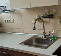 Konyha egy kétszobás lakásban mosogatóval, kerámia főzőlappal és kosárral az ablak mellett.