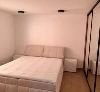 Világos hálószoba egy kétszobás lakásban, fa hatású padlóval és kényelmes ággyal.