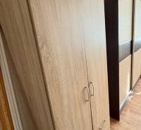 Szekrény garzonlakásban, fa mintázatú padlóval és tolóajtókkal.