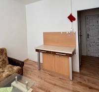 Garzonlakás kanapéval, üvegasztallal és fa mintázatú padlóval.