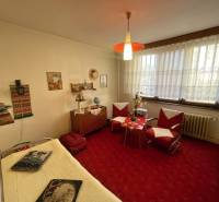 Szoba egy háromszobás lakásban régi bútorokkal, piros szőnyeggel és dekorációkkal.