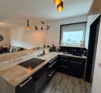 Konyha fekete bútorokkal, bárpulttal és fa dekorációjú padlóval egy háromszobás lakásban.