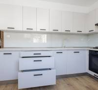 Konyha egy háromszobás lakásban fehér szekrényekkel és fa dekor padlóval.