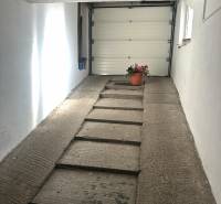 Családi ház garázsa beton rámpával és virágcseréppel a fal mellett.