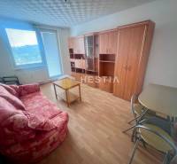 Nappali egy háromszobás lakásban kanapéval, asztallal és szekrénnyel, világos padlóval.