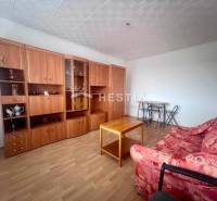 Nappali egy háromszobás lakásban piros kanapéval és fa nappali szekrénnyel.