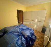 Szoba szekrénnyel, radiátorral és letakart bútorral egy háromszobás lakásban.